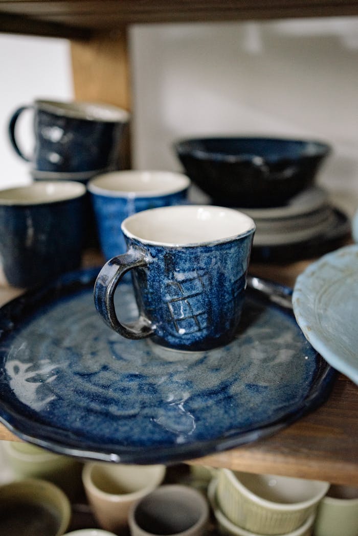 A collection of handcrafted blue ceramic dishes and cups on wooden shelves, showcasing artisanal kitchenware.